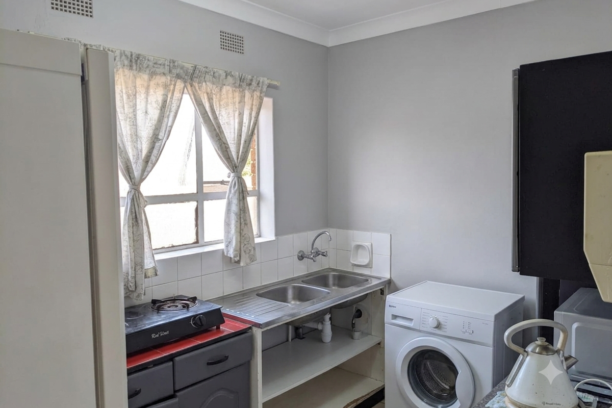 Compact kitchen area featuring a double stainless steel sink, tiled splashback, and built-in cabinetry with space for laundry appliances.