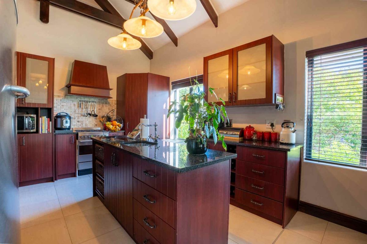 A well-appointed kitchen featuring dark wood cabinetry, granite countertops, a central island, and exposed timber beams, offering a warm and functional cooking space.