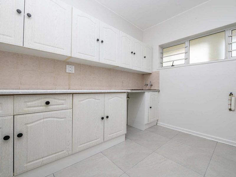 A functional kitchen space featuring white built-in cabinetry, tiled backsplash, and tiled flooring, offering a clean canvas for potential updates.