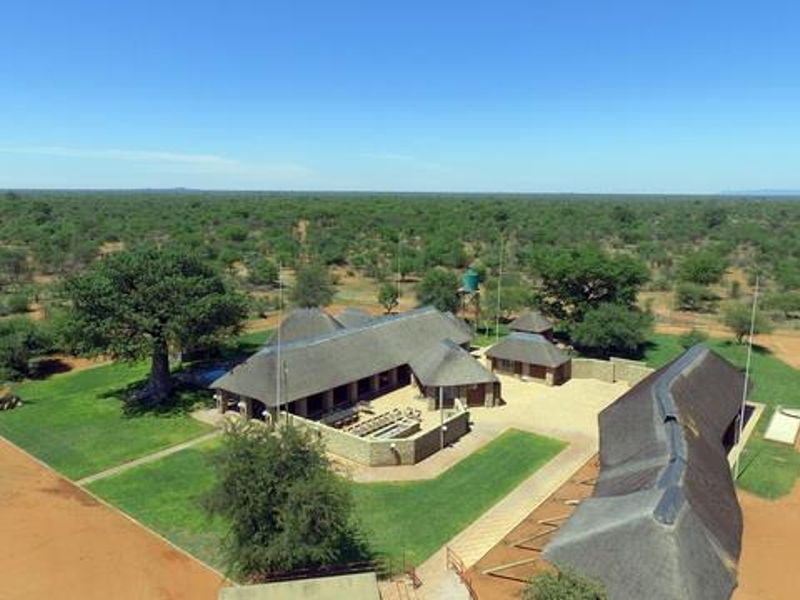 Aerial view of a farm property featuring multiple thatched-roof buildings, manicured lawns, and expansive surrounding bushveld landscape.