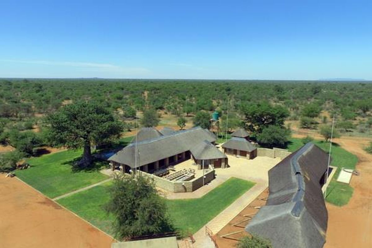 Aerial view of a farm property featuring multiple thatched-roof buildings, manicured lawns, and expansive surrounding bushveld landscape.