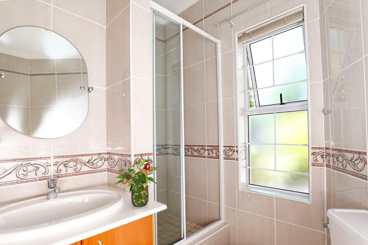 A functional bathroom featuring a built-in vanity with basin, a glass-enclosed shower, and tiled walls with decorative border accents.
