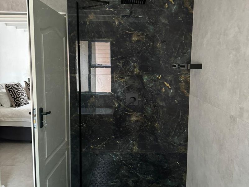 Modern bathroom featuring a walk-in shower with striking black marble-effect wall tiles, black hexagonal floor tiling, and contemporary black fixtures.
