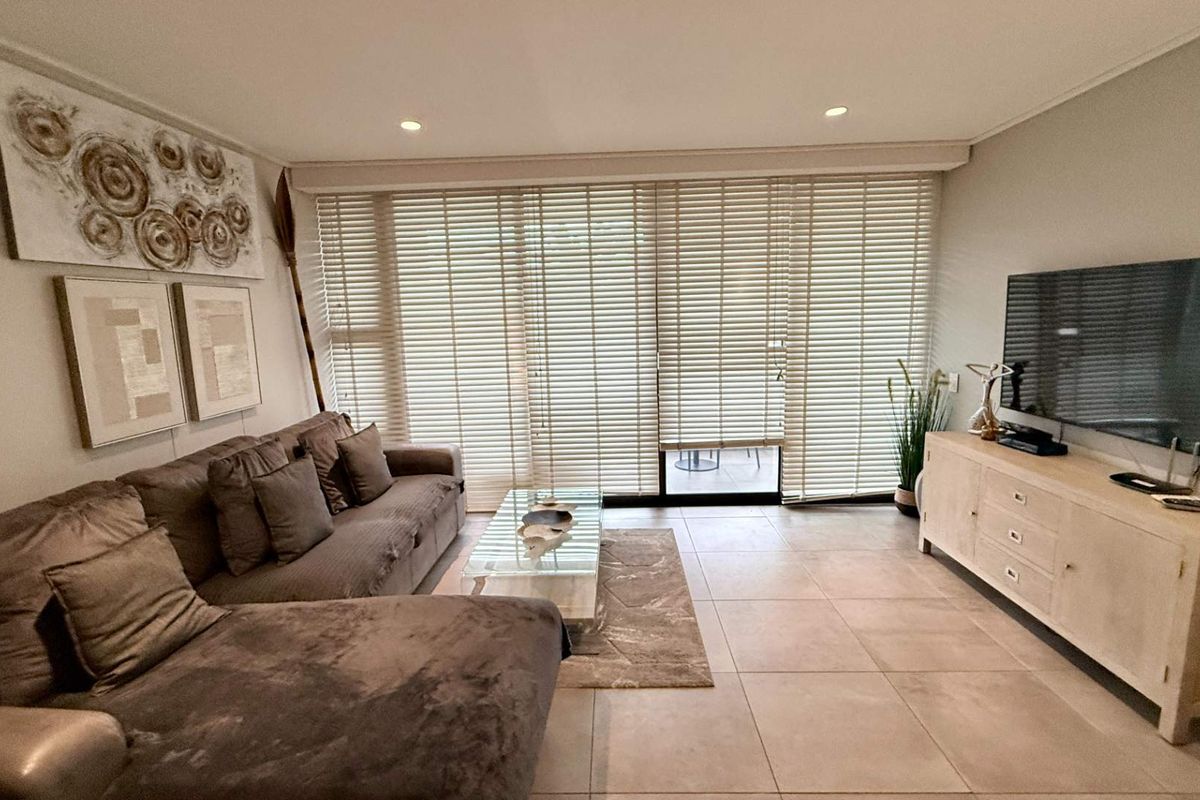A well-maintained living room featuring large format floor tiles, recessed lighting, and a sliding glass door with venetian blinds leading to an outdoor area.