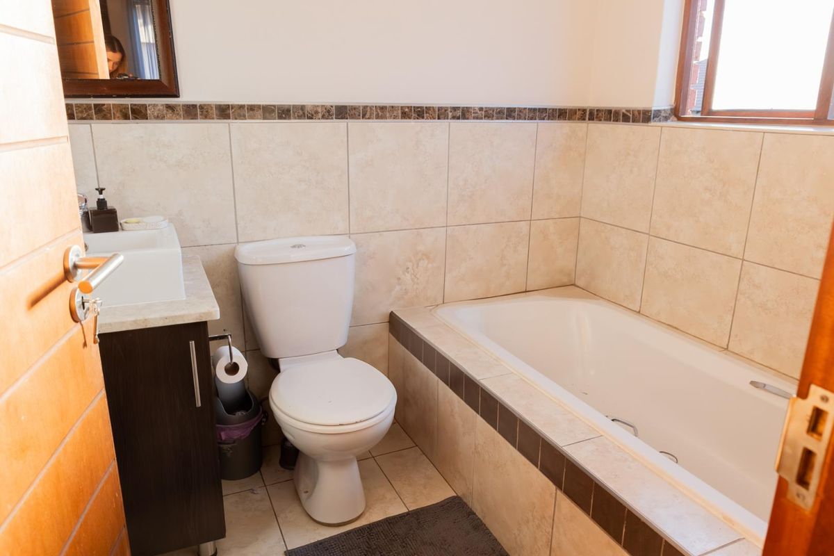 A functional bathroom featuring a built-in bathtub, a modern vanity with a basin, and a standard toilet with neutral wall and floor tiling.