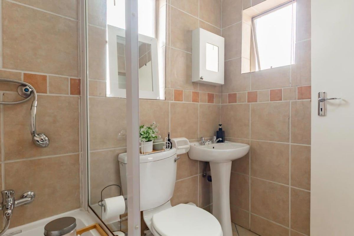 A compact bathroom featuring a pedestal basin, toilet, and a shower enclosure with tiled walls and flooring.