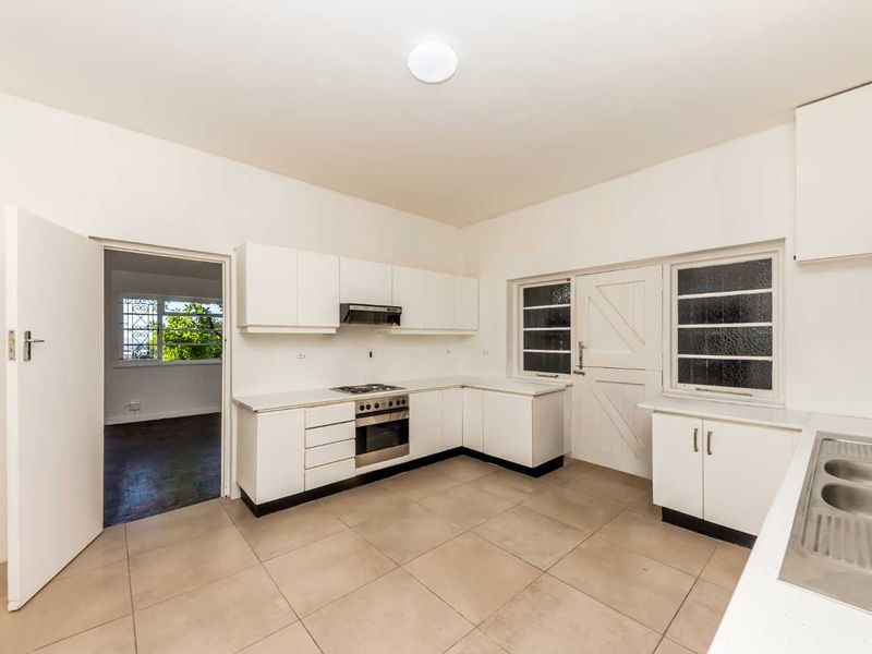 A functional, empty kitchen featuring white built-in cabinetry, a stainless steel oven with extractor fan, double sink, and neutral tiled flooring.
