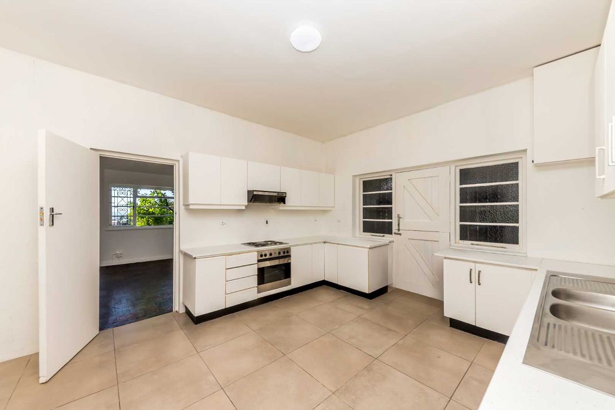A functional, empty kitchen featuring white built-in cabinetry, a stainless steel oven with extractor fan, double sink, and neutral tiled flooring.
