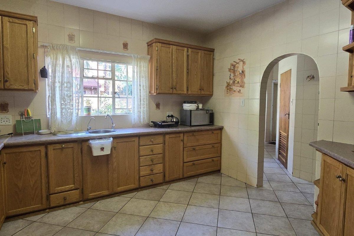 A functional kitchen featuring traditional wooden cabinetry, tiled backsplash, laminate countertops, and a built-in oven, with an arched entrance to the hallway.