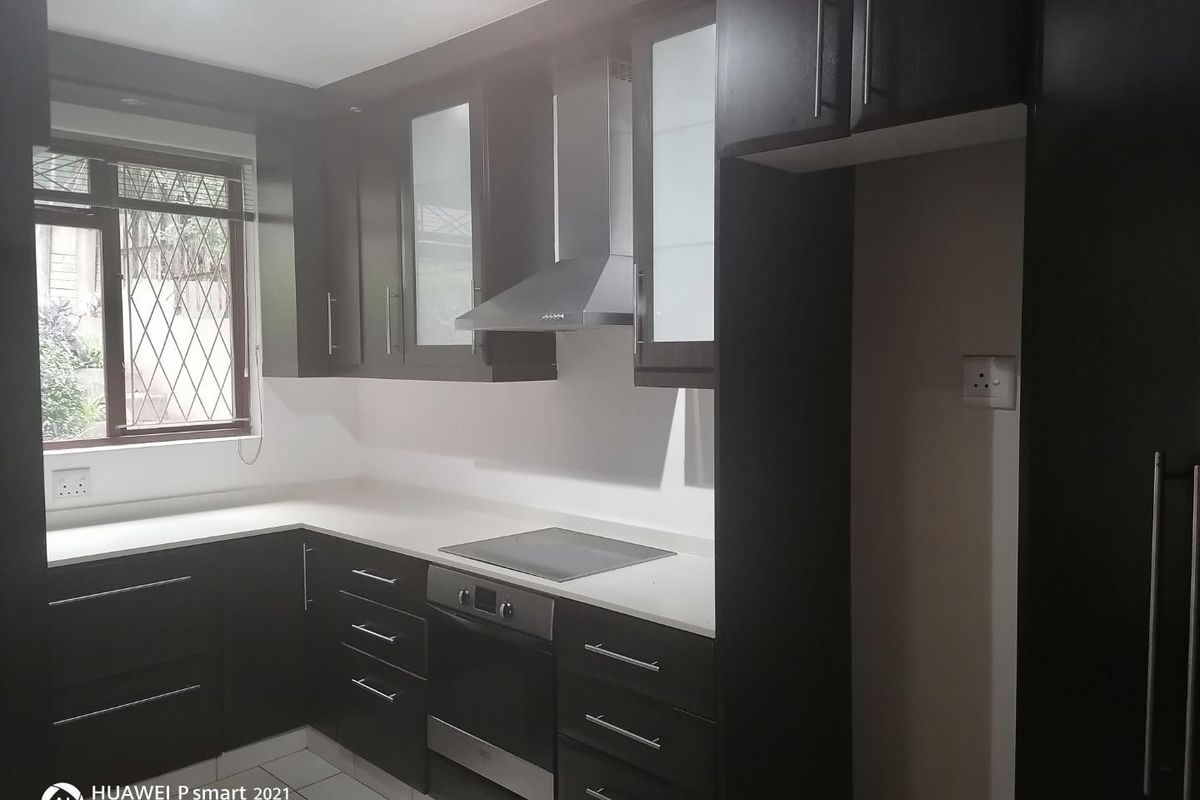 Modern kitchen featuring dark wood cabinetry, stone countertops, built-in oven, electric hob, and stainless steel extractor fan.