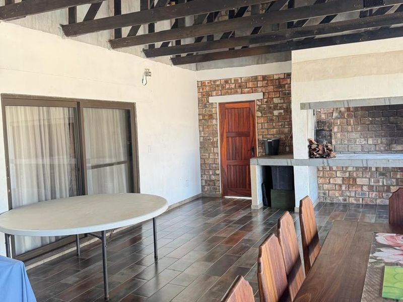 Spacious covered patio featuring exposed timber roof trusses, tiled flooring, and a built-in brick braai, ideal for outdoor entertaining.