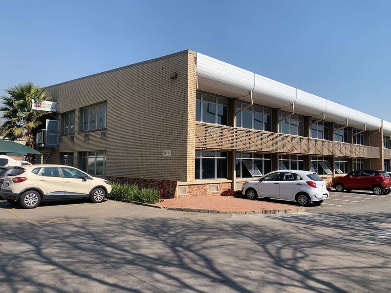 A two-story industrial office building featuring a brick facade, aluminium windows, and an adjacent paved parking area.