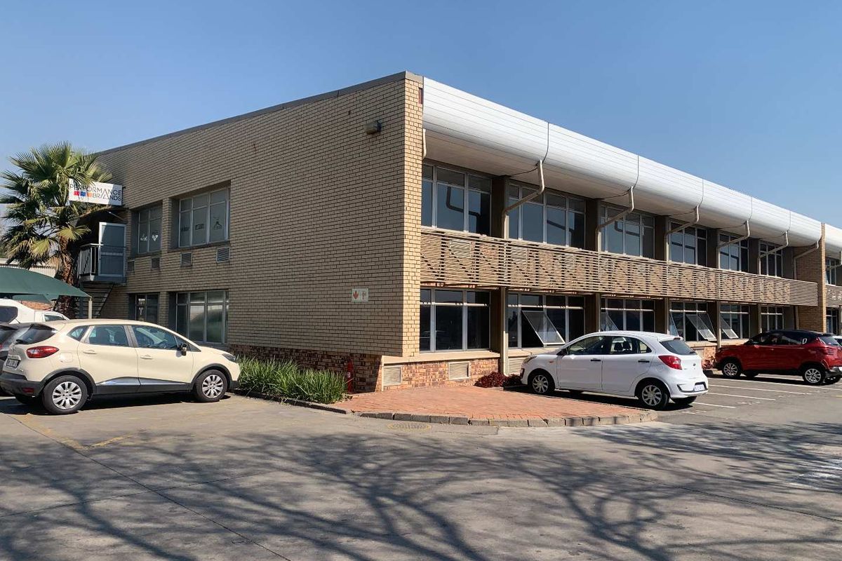 A two-story industrial office building featuring a brick facade, aluminium windows, and an adjacent paved parking area.