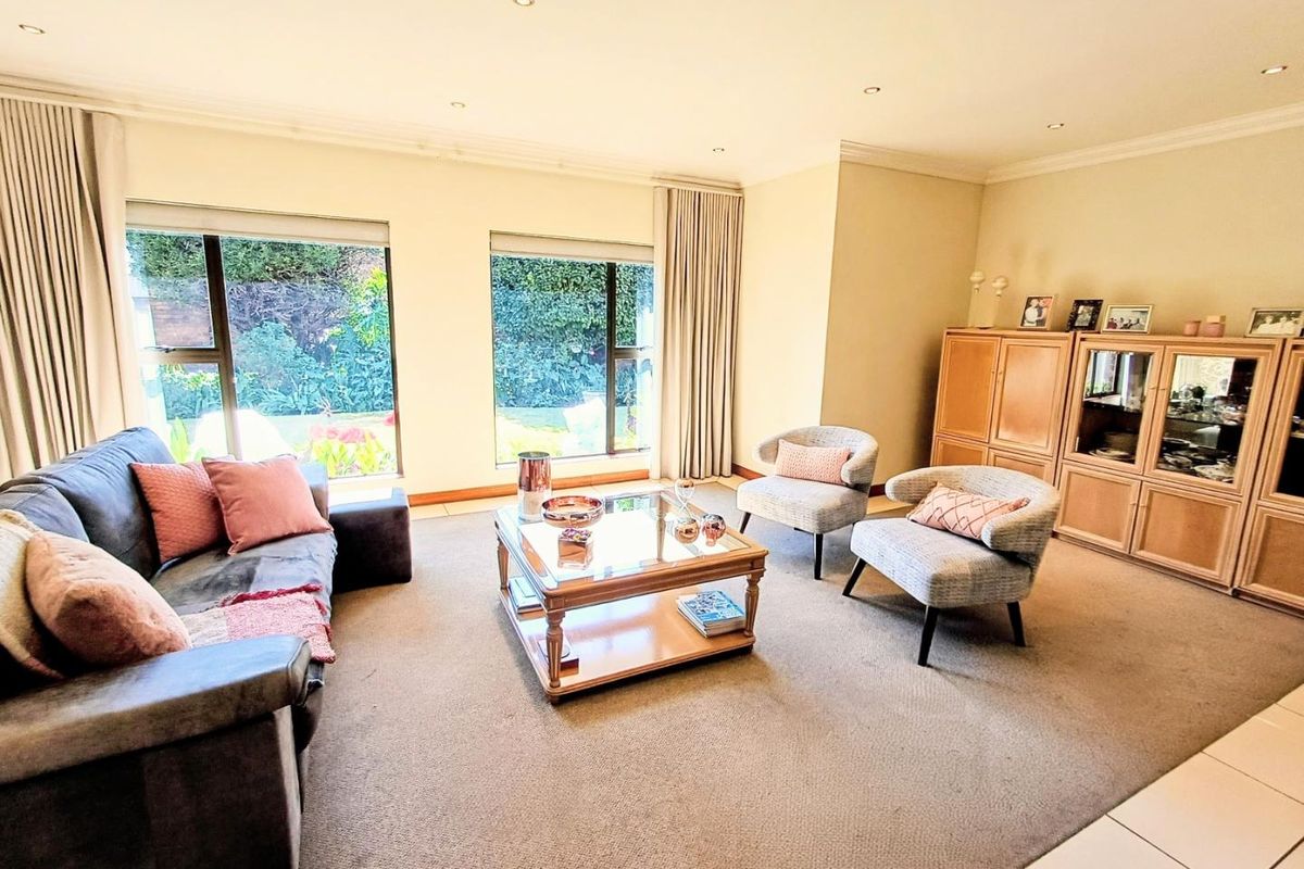A spacious living room featuring large windows with garden views, recessed downlighting, and neutral carpeting, offering a comfortable and well-lit living space.