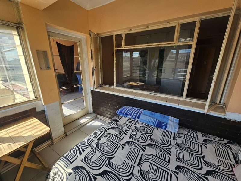 A bedroom featuring tiled floors, brick wall accents, and large windows providing natural light, with direct access to an outdoor area.