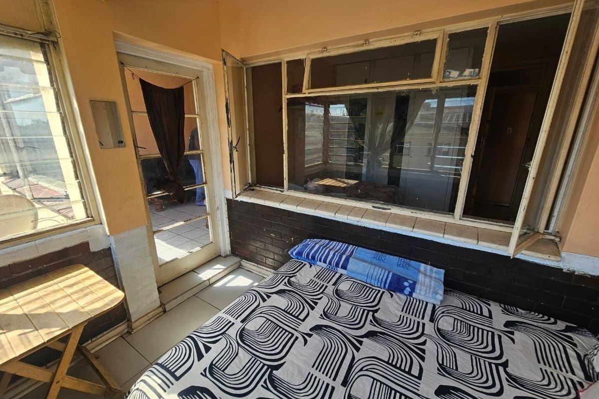 A bedroom featuring tiled floors, brick wall accents, and large windows providing natural light, with direct access to an outdoor area.