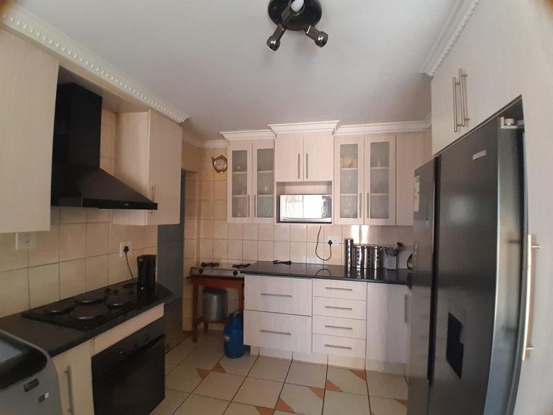 Functional kitchen featuring built-in cabinetry, granite countertops, electric hob, oven, extractor fan, and tiled flooring with a classic backsplash.