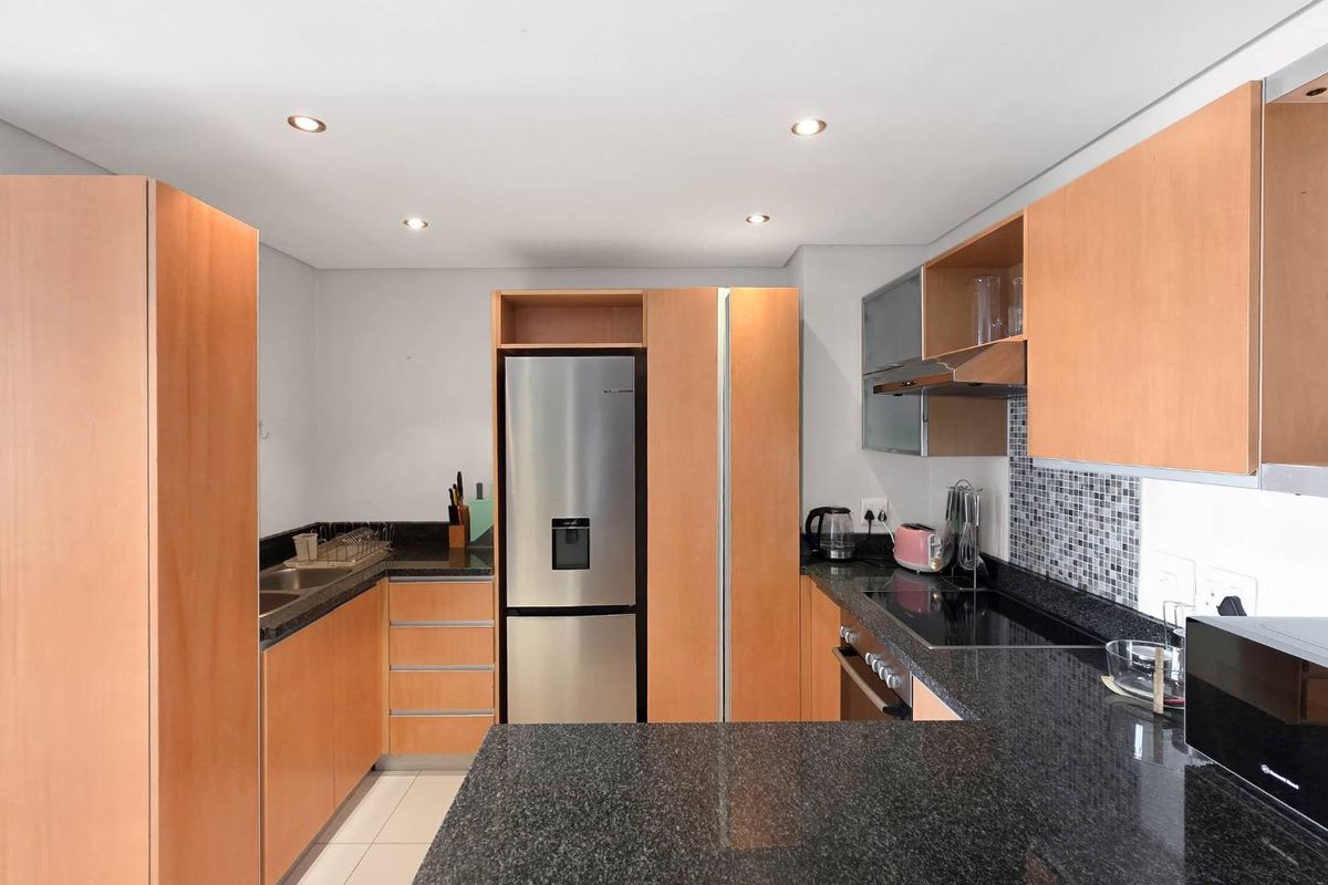 A functional kitchen featuring light wood cabinetry, dark granite countertops, a mosaic tile backsplash, and integrated stainless steel appliances.