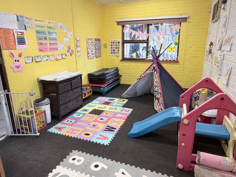 A multi-purpose room featuring exposed brick walls and a window, currently utilized as a play area with carpeted flooring.
