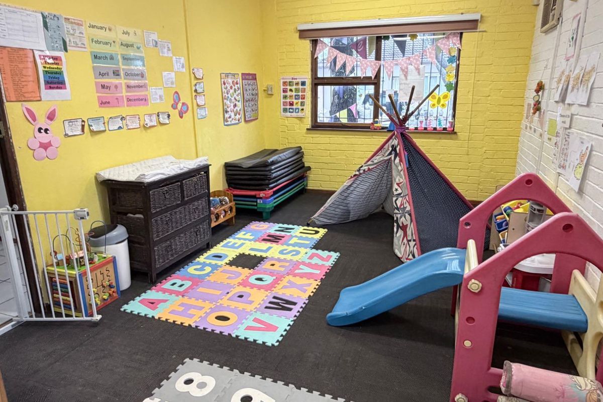 A multi-purpose room featuring exposed brick walls and a window, currently utilized as a play area with carpeted flooring.