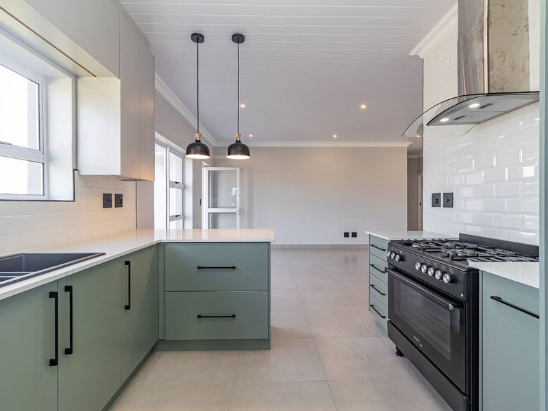 Modern kitchen featuring sage green cabinetry, quartz countertops, subway tile backsplash, and a gas stove, flowing into an open-plan living area.