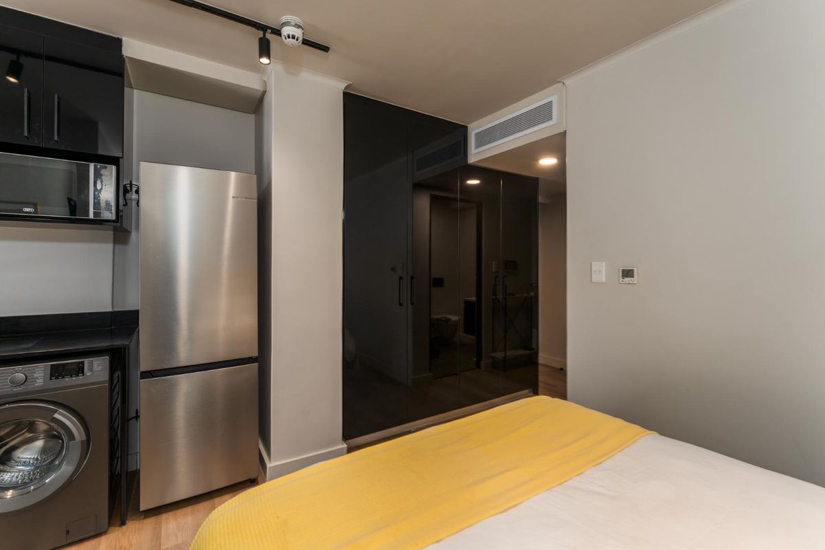 A modern bedroom featuring built-in high-gloss cabinetry, integrated microwave, and ducted air conditioning, offering a sleek and functional living space.
