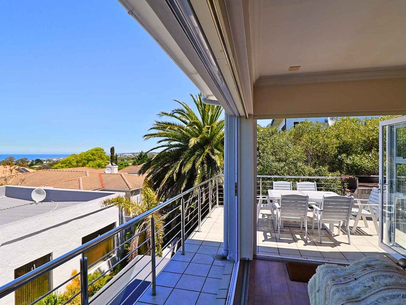 Spacious covered balcony featuring tiled flooring and a stainless steel balustrade, offering elevated views of the surrounding neighborhood and distant coastline.