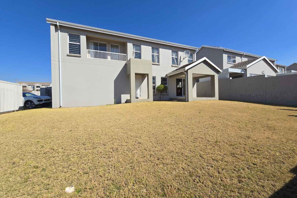 Rear view of the two-story house featuring a spacious lawn, a balcony, and boundary walls.