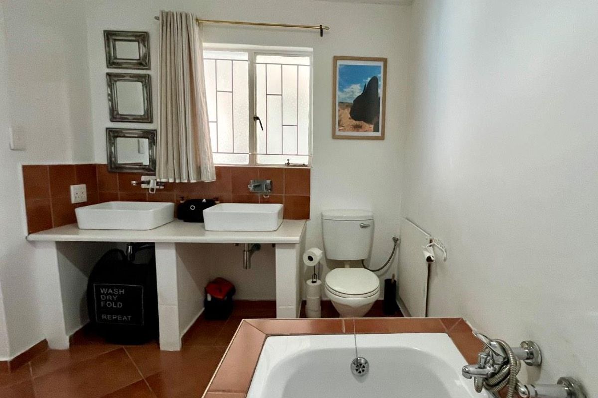A functional bathroom featuring a built-in vanity with dual vessel sinks, a standard toilet, and a tiled bathtub with chrome fixtures.