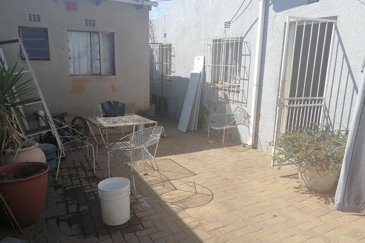 A paved rear courtyard area featuring security bars on windows and a security gate, showing signs of weathered exterior wall finishes.