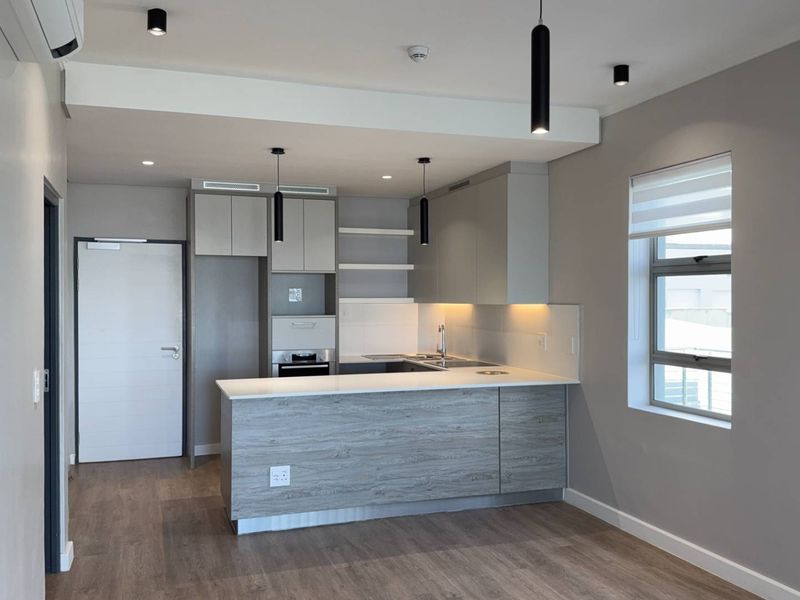 Modern open-plan kitchen featuring sleek cabinetry, stone countertops, integrated appliances, and contemporary lighting, set within a neutral, well-maintained living space.