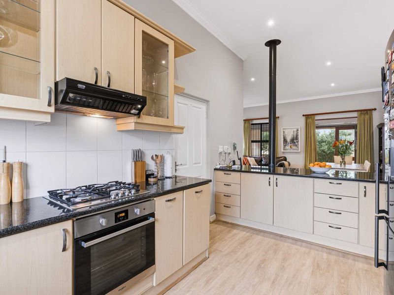 Open-plan kitchen featuring light wood cabinetry, granite countertops, built-in oven, gas hob, and a breakfast bar flowing into the adjacent living and dining area.
