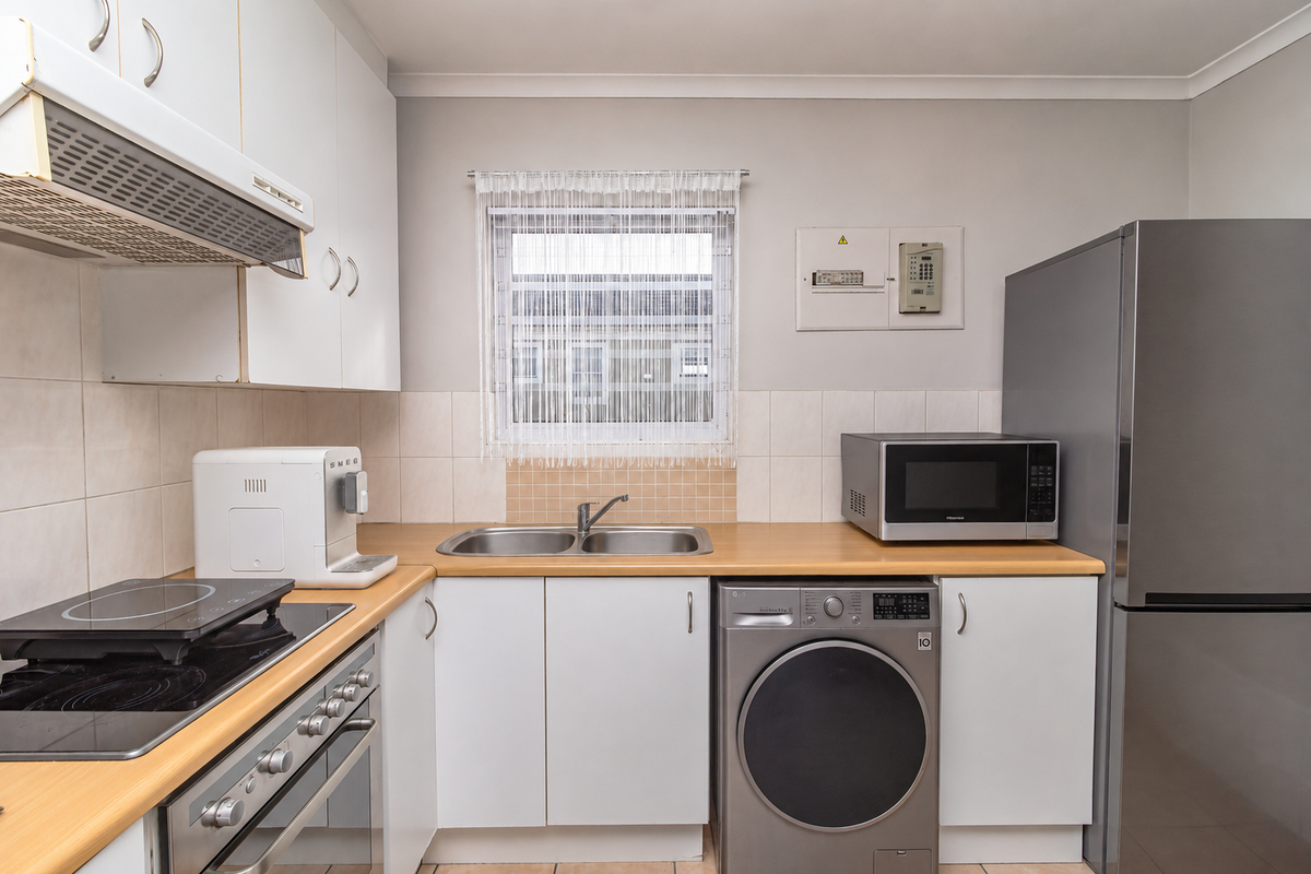 A functional kitchen featuring white cabinetry, laminate countertops, a built-in oven with hob, and integrated space for a washing machine.