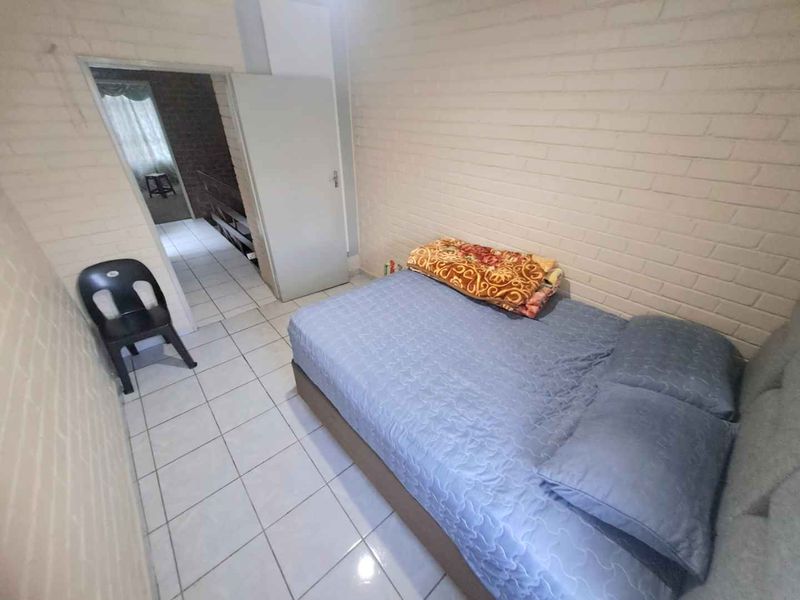 A bedroom featuring painted brick walls and tiled flooring, with an internal door leading to an adjacent space.