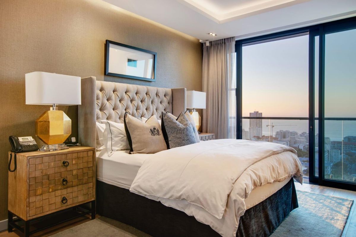 A well-appointed bedroom featuring textured wall finishes, recessed ceiling lighting, and a large sliding glass door opening to a balcony with city and ocean views.
