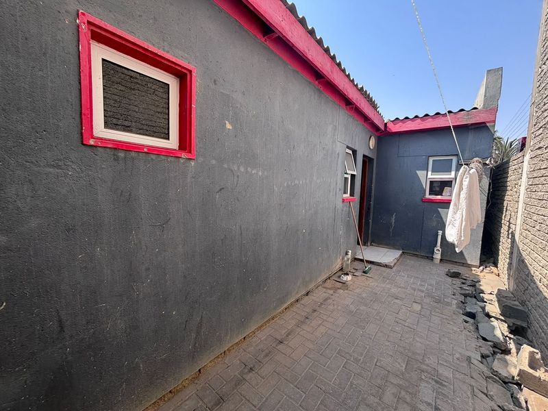 Rear exterior view of the townhouse featuring a paved courtyard area, dark grey walls with red trim, and multiple window access points.