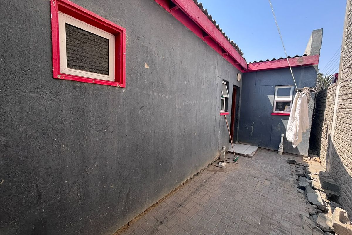 Rear exterior view of the townhouse featuring a paved courtyard area, dark grey walls with red trim, and multiple window access points.