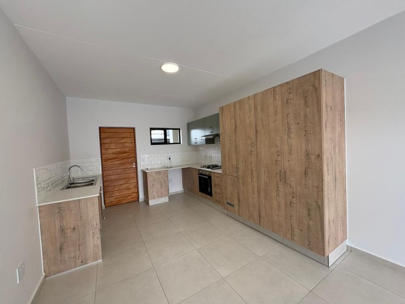 Modern kitchen featuring light wood-grain cabinetry, stone countertops, subway tile backsplash, and integrated stainless steel appliances, set against neutral walls and tiled flooring.