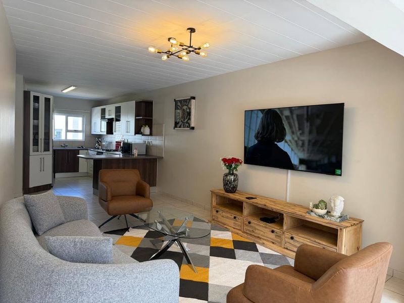 Open-plan living area featuring a modern kitchen with cabinetry and island, flowing into a comfortable lounge space with tiled flooring and contemporary lighting.