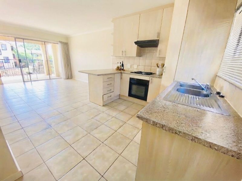 Open-plan kitchen and living area featuring light wood-finish cabinetry, laminate countertops, built-in appliances, and ceramic floor tiles leading to a patio.