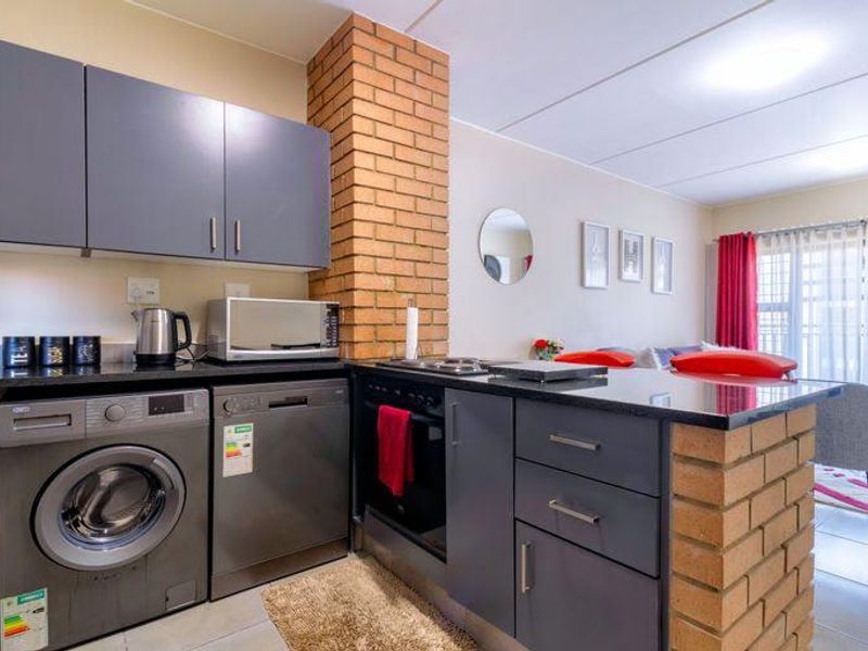 Modern open-plan kitchen featuring dark grey cabinetry, a brick feature pillar, integrated oven, and hob, seamlessly flowing into the living area.