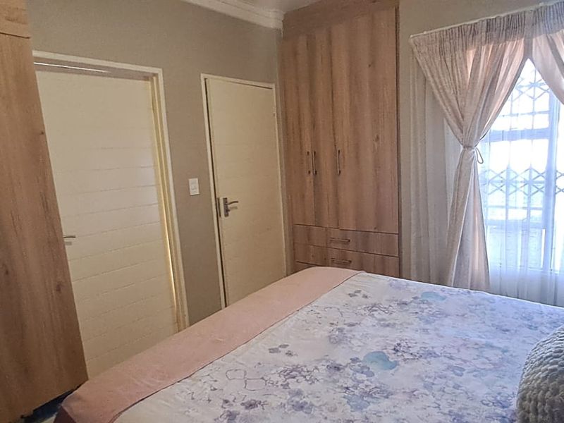 A well-maintained bedroom featuring light wood-finish built-in cupboards, neutral wall tones, and a window fitted with a security gate.