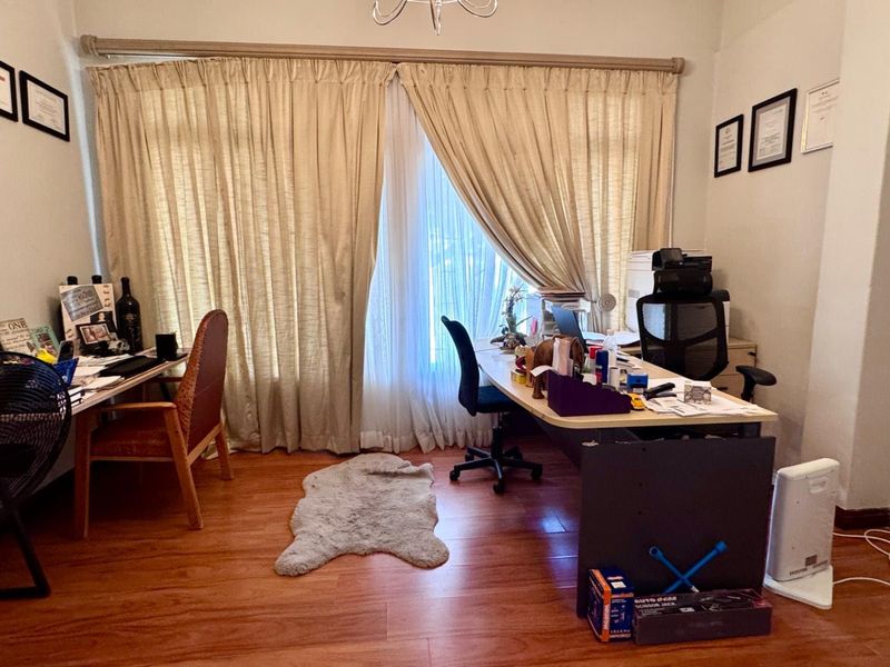 A functional home office space featuring laminate wood flooring and large window treatments, providing a dedicated area for work or study.