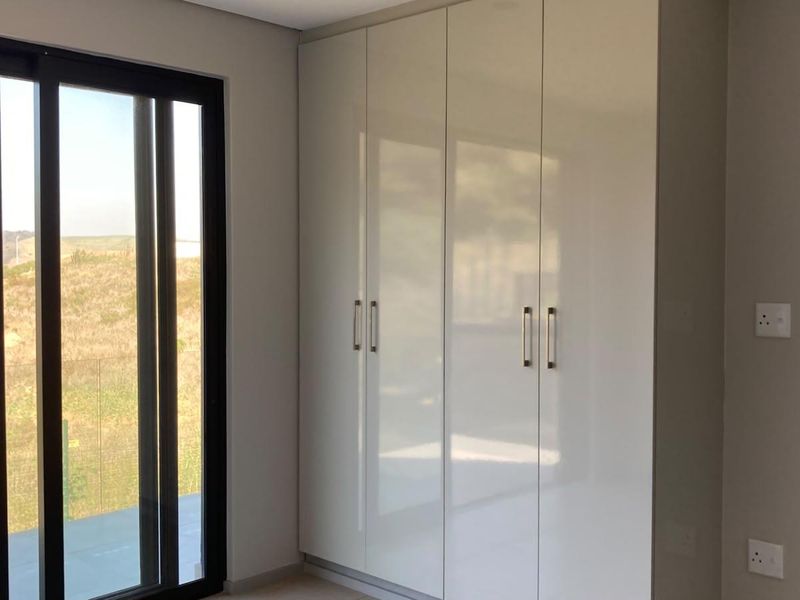 A bright bedroom featuring modern high-gloss built-in wardrobes and a large sliding glass door providing access to an outdoor area.