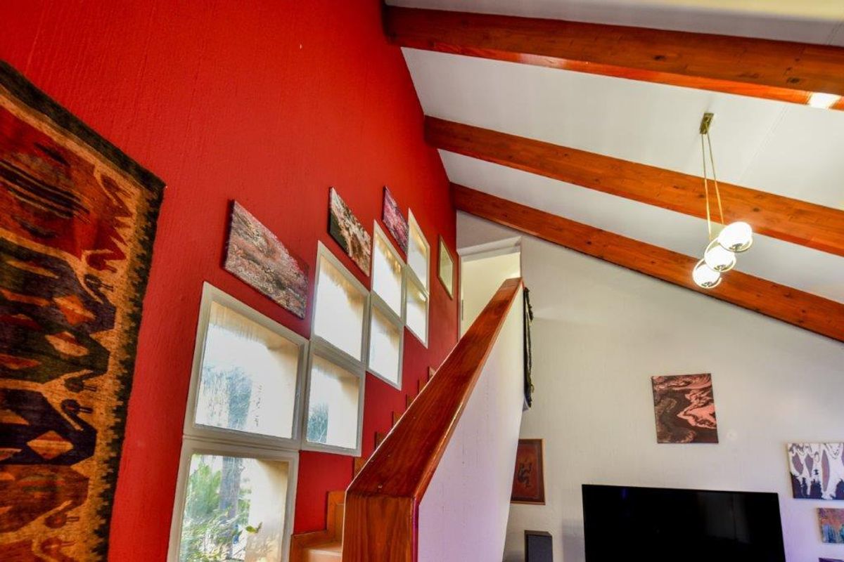 A living area featuring high vaulted ceilings with exposed timber beams, a striking red accent wall, and a staircase with a wooden handrail.