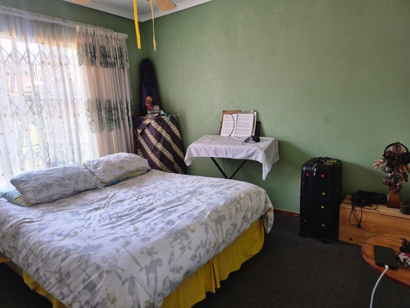 A bedroom featuring a ceiling fan and a window with a security gate, providing a functional space with potential for cosmetic updates.