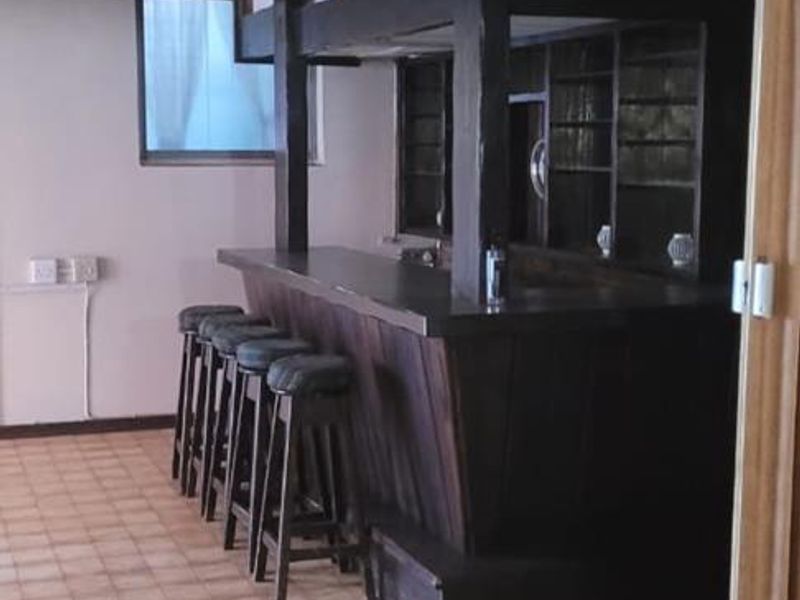A dedicated bar area featuring a built-in timber counter, integrated shelving, and exposed ceiling beams, offering a classic entertainment space.