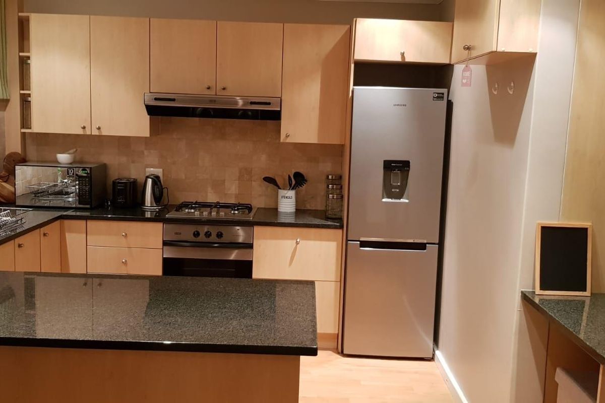A functional kitchen featuring light wood cabinetry, granite countertops, a built-in oven, gas hob, and an integrated extractor fan.
