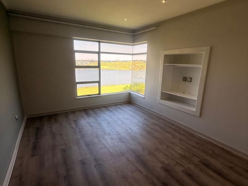 An empty living room featuring modern laminate flooring, recessed shelving, and a large corner window offering scenic water views.