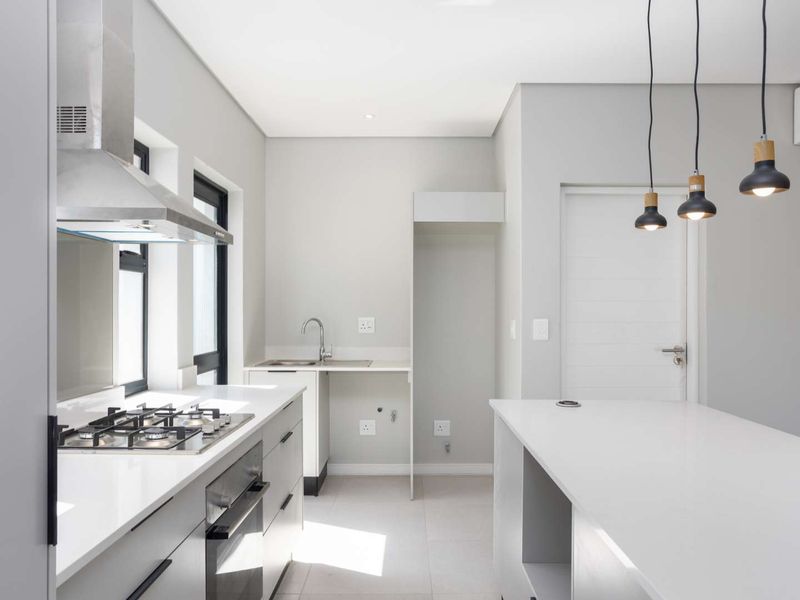 Modern kitchen featuring sleek grey cabinetry, quartz countertops, a gas hob, built-in oven, and integrated stainless steel extractor fan in a clean, minimalist space.